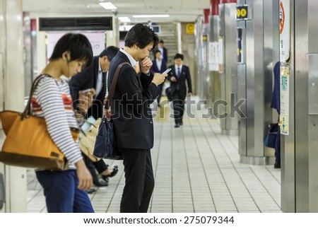 OSAKA, JAPAN - OCTOBER 27: People on a platform in Osaka, Japan on October 27, 2014. Unidentified Japanese male uses his device while waits for a train on a plateform