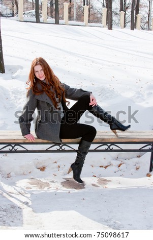 young beautiful woman on a bench in winter in a park