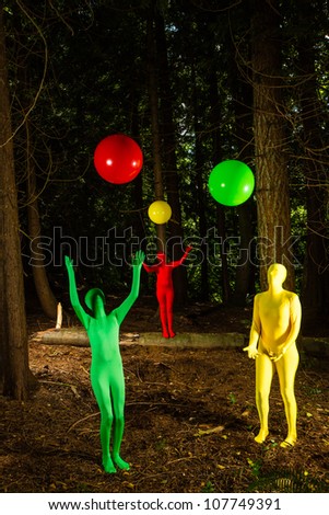 Strange, colorful people playing with balls in a dark wooded forest.