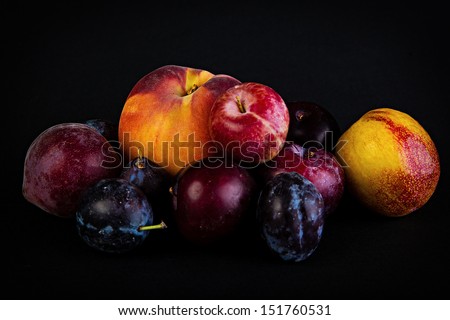 A pile of fresh, dark fruits including plums and peaches.