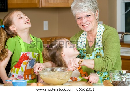 Happy Family featuring a friendly Grandma baking cookies in a home kitchen with her two Grandchildren.