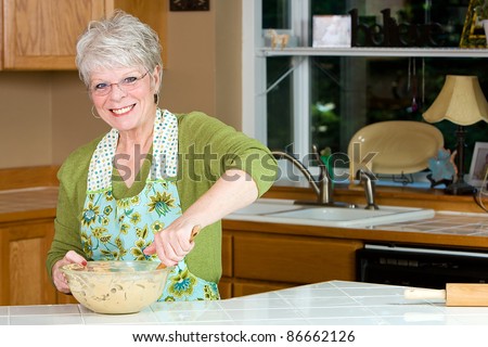 Friendly mature woman with a nice smile and white hair baking cookies in the kitchen.
