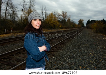 A pretty woman on a fall day standing near railroad tracks under a dark cloudy sky.