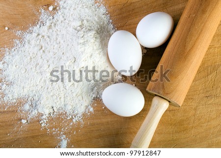 Baking ingredients including fresh eggs, flour and a rolling pin on a cutting board.