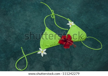Green bikini top floating in pool with Pulmeria flowers and a hibiscus flower