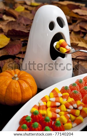Ghost eating candy corns with a spoon surrounded by colorful fall leaves and Halloween candy