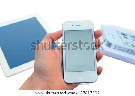 BARCELONA, SPAIN Â?Â? APR 08, 2014: A male hand holding a white Apple Iphone device above and an Apple Ipad device and Iphone case on the background, isolated on white background.