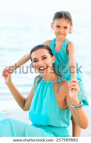Happy family mother and girl resting on the beach in beautiful turquoise azur dresses