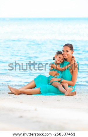 Happy family mother and girl resting on the beach in beautiful turquoise azure dresses
