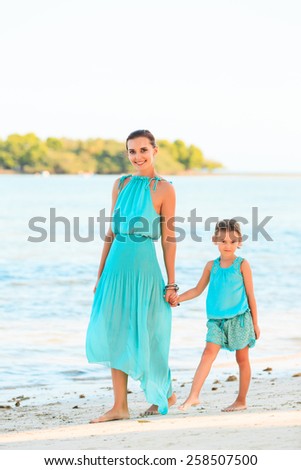 Happy family mother and girl resting on the beach in beautiful turquoise azure dresses