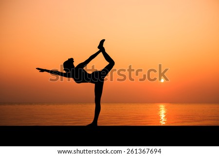 Silhouette of sport slim woman making yoga poses on the beach with Seaview in sunset