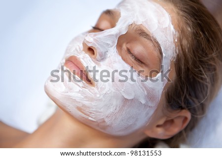 Beautiful happy woman in spa making face mask treatment