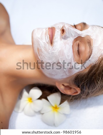 Beautiful happy woman in tropical spa making face mask treatment