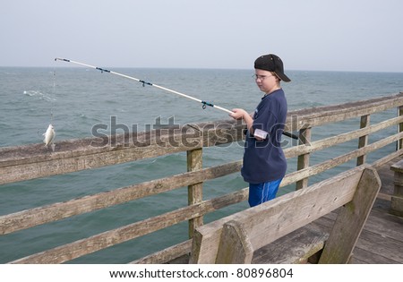 A boy fishing off a pier at the ocean