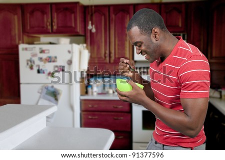 Young black African American man eating food from a bowl in a home kitchen