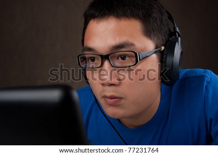 closeup of young asian man playing games on laptop computer on gray background