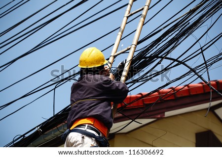 An unidentified male worker on bamboo ladder is repairing telephone line near the community.