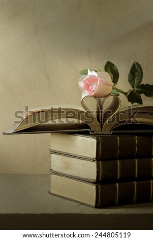Still life art photography love concept with pink rose vintage book pages love heart sign on grunge selective focus