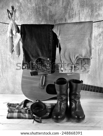 Hanging jeans and corns with shirt and boots over acoustic guitar and grunge background still life style black and white version