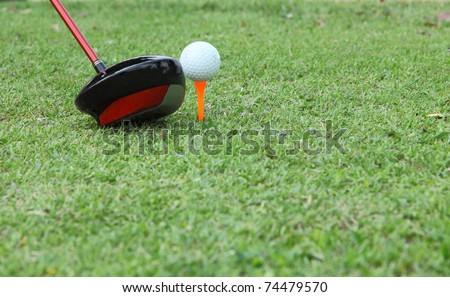 Close-up of golf ball on tee with driver ready to tee off, blur grass at foreground.