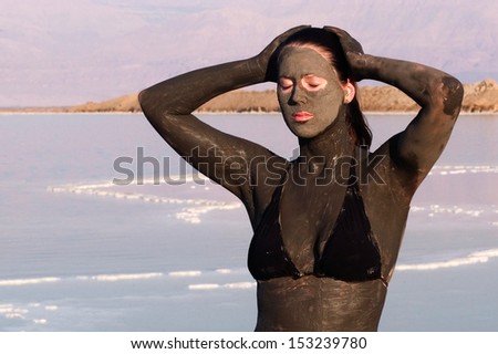 A young woman in a bathing suit is enjoying the natural mineral mud sourced from the Dead Sea,  Israel.