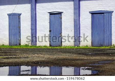 Three old purple doors and puddle reflection.