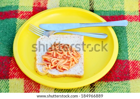 Caned spaghetti on bread slice in a yellow plate with knife and fork over a picnic blanket. Concept photo of food, preserved,outdoor, camping, survival,surviving,travel, vacation , poor.