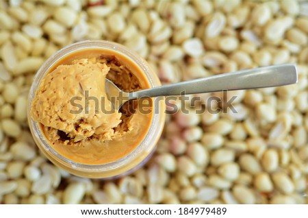 Crunchy peanut butter in jar with spoon with  dry roasted peanuts in the background. Concept photo of food