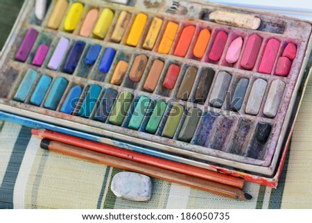 Panel set of  used colorful chalk colors with pencils and rubber on artist chair.