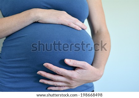 Close-up of unrecognizable pregnant woman with hands over tummy against Turquoise background.Concept photo of pregnancy, pregnant woman lifestyle and health care.copyspace