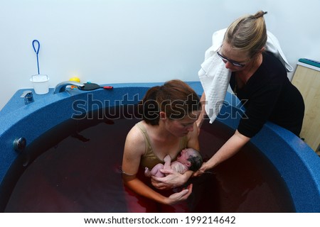 AUCKLAND - JUNE 07 2014:Woman holds her baby in a pool after natural water birth.Women have been using water in labour and birth for thousands of years.