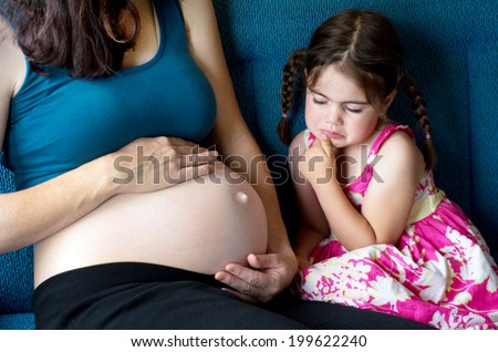 Sad little girl looks at her pregnant mother belly. Selfish child crying for not wanting a sibling.Concept photo of pregnancy, pregnant woman, family, issue, childhood, parenthood, motherhood.