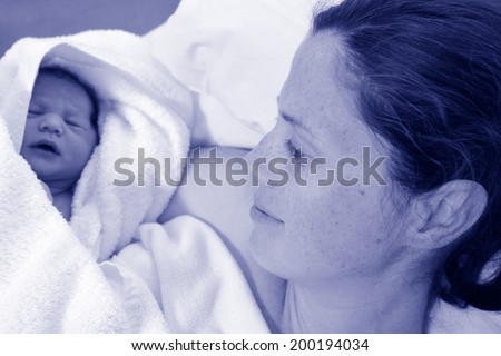 Mother looks at her newborn baby in bed immediately after a natural water birth labour. Concept photo of  pregnant woman, newborn, baby, pregnancy. (BW)