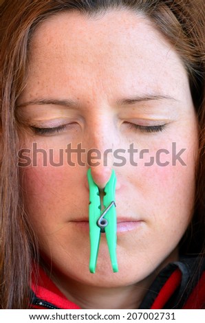 Young woman closing eyes with cloth peg on her nose. Concept  photo of  bad smell and odor.Head shot portrait. Close Up