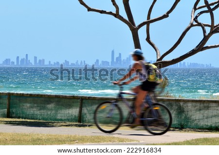 GOLD COAST - OCT 07 2014:Woman ride a bicycle under Surfers Paradise Skyline.It\'s one of Australia\'s iconic coastal tourist destinations, drawing 10 million tourists every year from all over the world