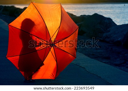 Silhouette of a little girl (age 04) with red umbrella during sunset.