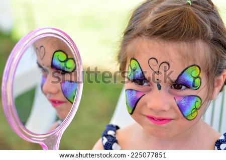 little girl getting with face painting looks at the mirror. Focus on face.
