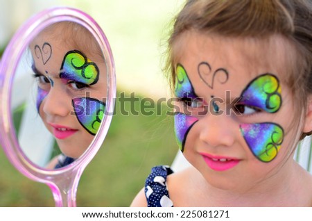 little girl getting with face painting looks at the mirror. Focus on mirror reflection