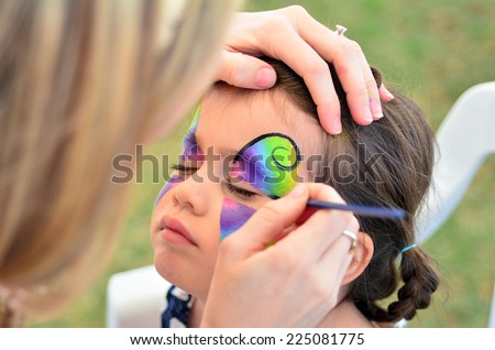 Young girl (age 5-6) getting her face painted like a butterfly by face painting artist. Real people. Copy space