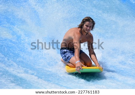GOLD COAST OCT 29 2014: Young man ride a surfing board on FlowRider. It is a water park attraction that simulate the riding of waves in the ocean