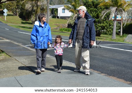 Young grandparents hold hand and walking with their granddaughter outdoor during the autumn.
