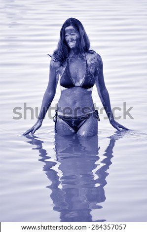 A young woman in a bathing suit is enjoying the natural mineral mud sourced from the Dead Sea,  Israel.