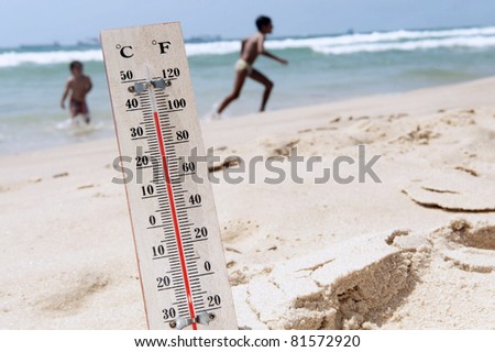 A temperature scale on a beach with people in the background shows high temperature during a heat wave. Concept photo of heat wave , warm weather, global warming, high temperatures, climate change.