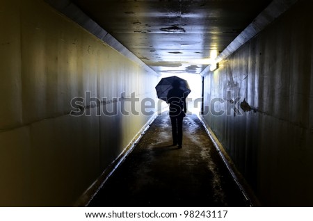 Silhouette of woman holding an umbrella and walking in a tunnel. Light at End of Tunnel concept.