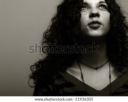 A low-key, black and white portrait about an attractive lady with white skin and long wavy hair who is looking up and desires something