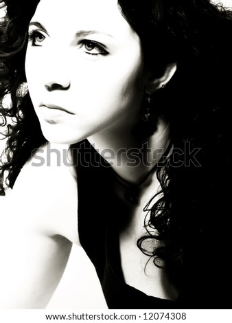A high-key, black and white portrait about an attractive lady with white skin and long wavy hair who has a charming look and who wears a nice dark dress