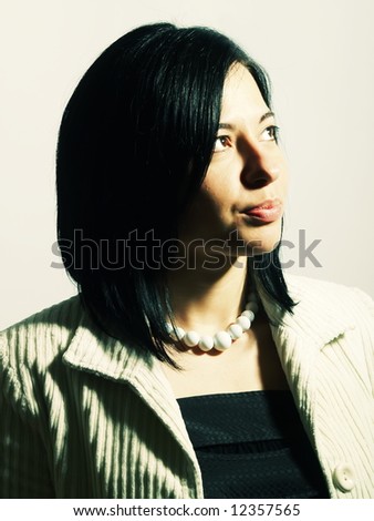A high-key portrait about a young attractive lady with black hair who is looking up and she is dreaming. She is wearing a white coat, a black dress and a white necklace.
