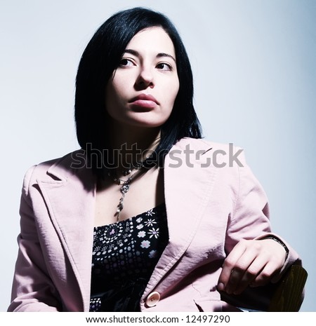 A portrait about an elegant trendy woman with black hair who is sitting on a chair, she is looking up and she is thinking. She is wearing a nice dress, a stylish necklace and a pink coat.