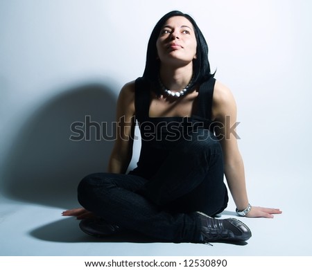 A portrait about an attractive trendy girl with black hair who is sitting, she is spreading her arms on ground, she is looking up and she is admiring something.