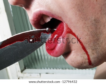 A portrait about an attractive guy who is taking a knife and he is trying to take his piercing out of his tongue.